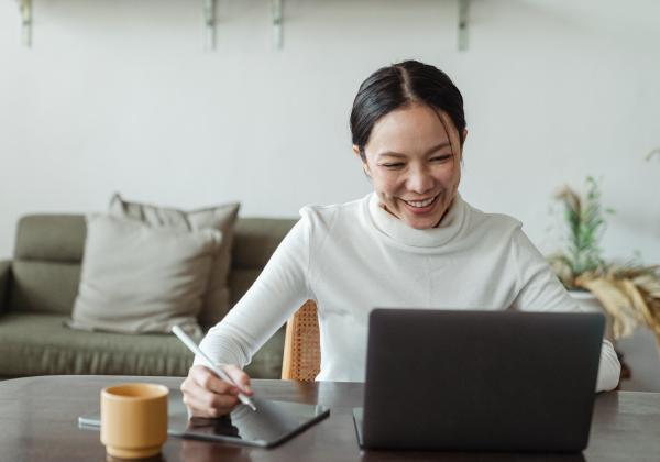 Women typing on a laptop with tablet next to her